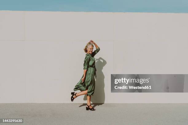 smiling mature woman dancing on sunny day - frau kleid stock-fotos und bilder