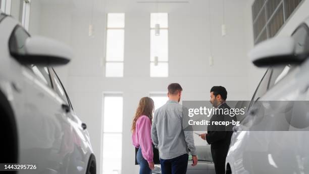 car salesman showing new cars to couple - used car salesman stock pictures, royalty-free photos & images