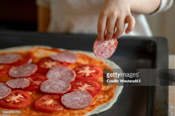 hand of boy preparing pizza with pepperoni in kitchen at home - pepperoni pizza stock-fotos und bilder