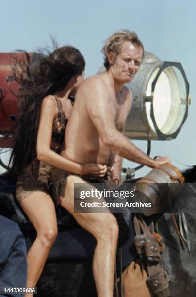 Charlton Heston and Linda Harrison on horseback filming the 1968 sci-fi film 'Planet of The Apes'. They are riding next to movie lights.