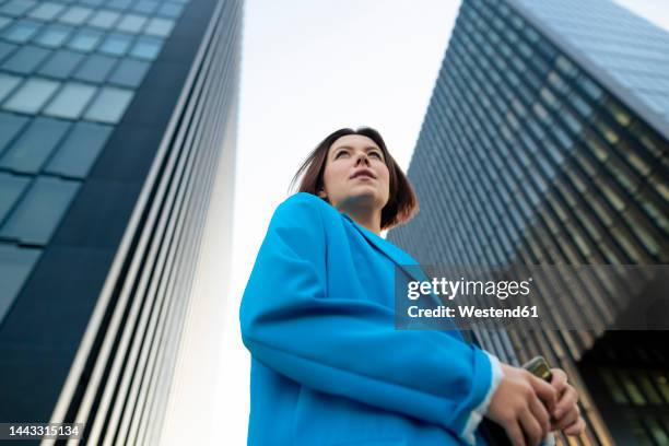 businesswoman wearing blue blazer standing near office building - vista de ángulo bajo fotografías e imágenes de stock