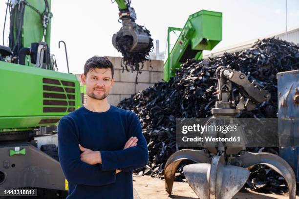 businessman with arms crossed standing in front of excavator - wiederverwertungsanlage stock-fotos und bilder