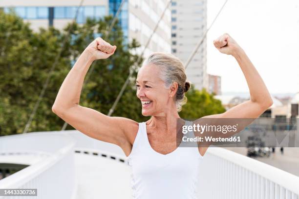 happy woman flexing muscles on footbridge - flexing arm stock-fotos und bilder