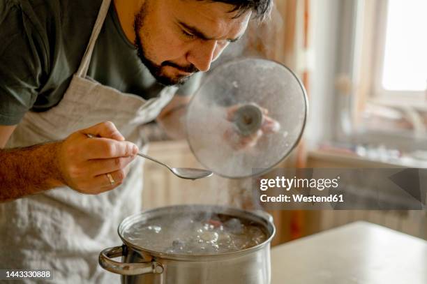 man tasting soup in kitchen at home - stew pot stock pictures, royalty-free photos & images