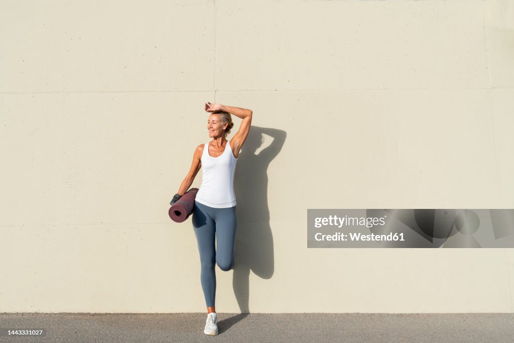 Woman With Yoga Mat Leaning On Cream Colored Wall High-Res Stock