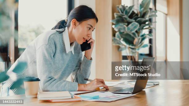 asian girl focus on laptop call mobile phone talk with colleague meeting work outside office on counter in a cafe. - asian woman on call stock pictures, royalty-free photos & images