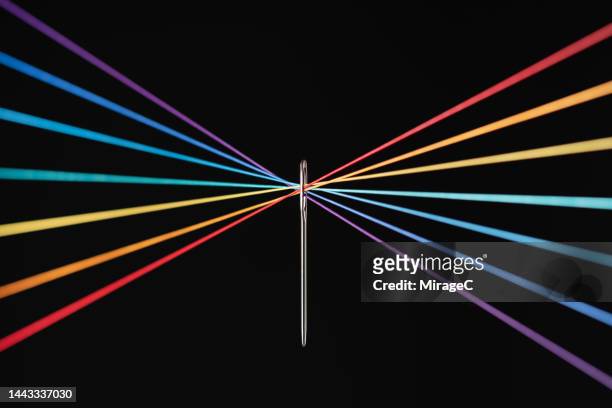 crossed rainbow colored strings converge through needle eyelet - haz de luz fotografías e imágenes de stock