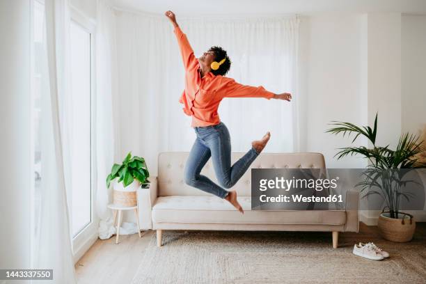 carefree freelancer wearing wireless headphones jumping at home office - 20 years old dancing stock pictures, royalty-free photos & images