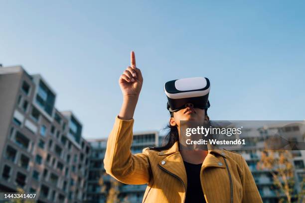 young woman gesturing with virtual reality simulator under blue sky - dedo índice fotografías e imágenes de stock