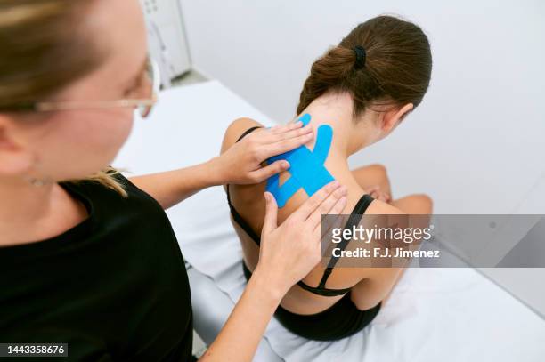 chiropractor placing elastic theurapetic tape on patient's neck - osteopath stock pictures, royalty-free photos & images