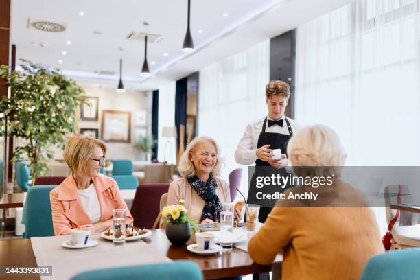 mujer mayor haciendo un pago sin contacto en un restaurante usando su teléfono celular - sentarse a comer fotografías e imágenes de stock