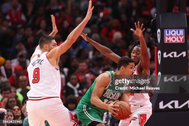 Malcolm Brogdon of the Boston Celtics passes the ball around Nikola Vucevic and Ayo Dosunmu of the Chicago Bulls during the second half at United...