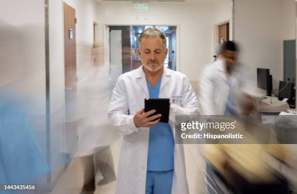 doctor using a tablet computer while working at a busy hospital - busy hospital lobby stock pictures, royalty-free photos & images