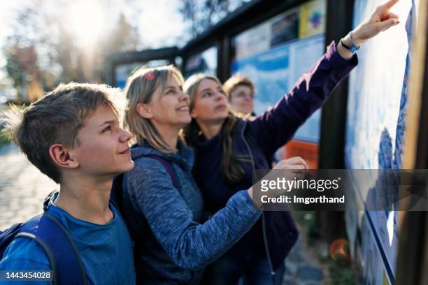 family standing by street hiking map in a small town in tatra mountains and planning the hiking route - boys and girls town stockfoto's en -beelden