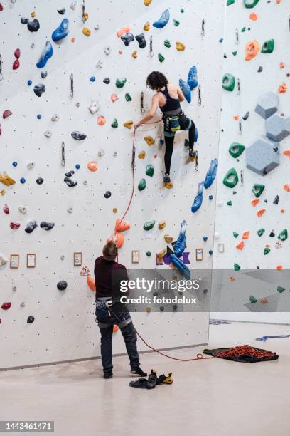 donna che pratica l'arrampicata su roccia in una palestra di arrampicata indoor - messa in sicurezza foto e immagini stock