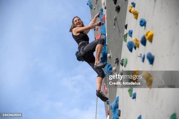 female climber with safety harness climbing on artificial rock wall outdoors - climbing wall stock pictures, royalty-free photos & images