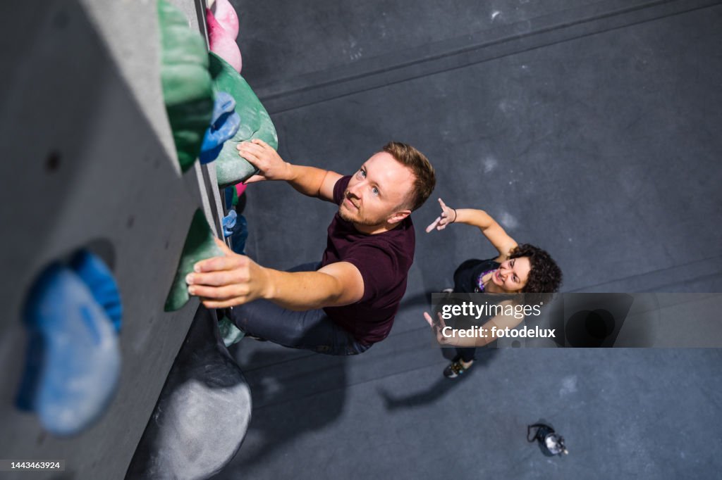 Man on the bouldering training with female instructor at sport climbing gym
