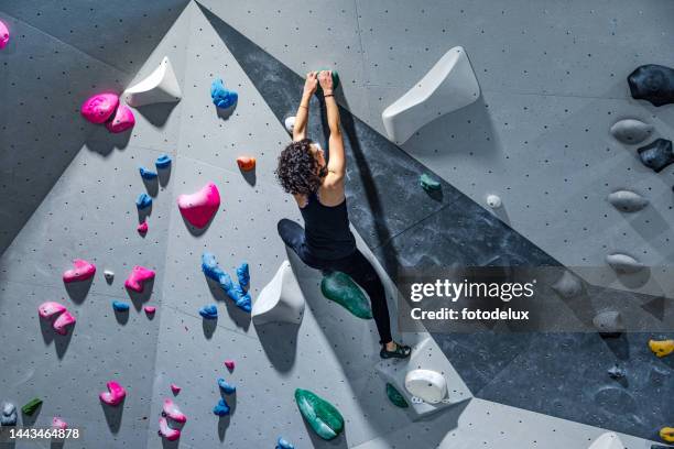 mujer con equipo de seguridad y entrenamiento de arnés en el muro de escalada artificial - escalar fotografías e imágenes de stock