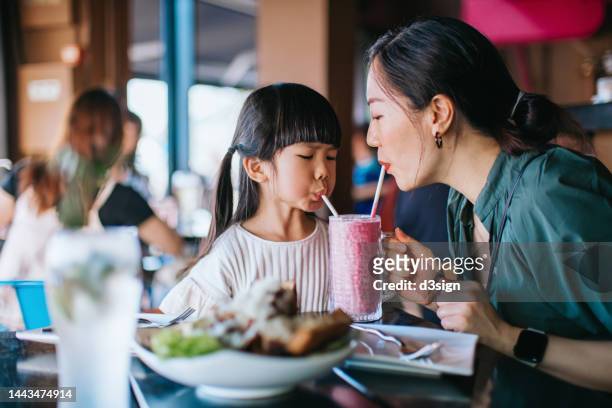 young asian mother and lovely little daughter sharing strawberry smoothie in restaurant. having a fun time while dining out together. mother and daughter bonding moment. family lifestyle. family eating out concept - asian family cafe stock-fotos und bilder
