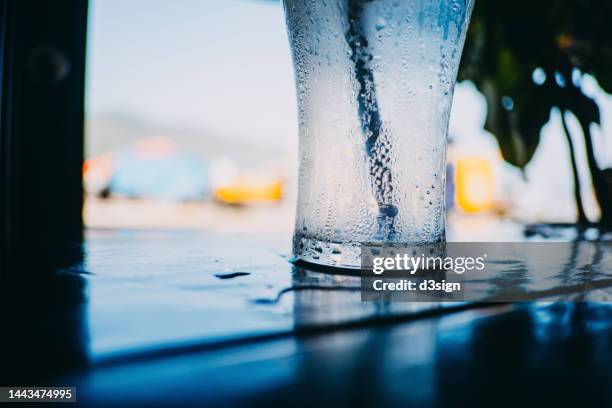 a glass of refreshing iced soda on table in an outdoor restaurant, against sunny blue sky - sparkling water glass stockfoto's en -beelden