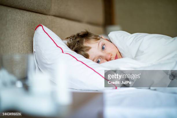 school age boy laying in bed with a flu - cold virus 個照片及圖片檔