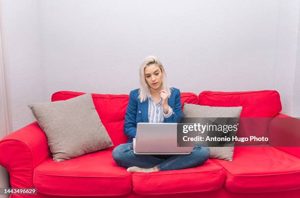 young blonde woman with platinum hair dressed in a blue blazer teleworking from home with the laptop. sitting on the couch. teleworking concept. - metallic blazer stock pictures, royalty-free photos & images