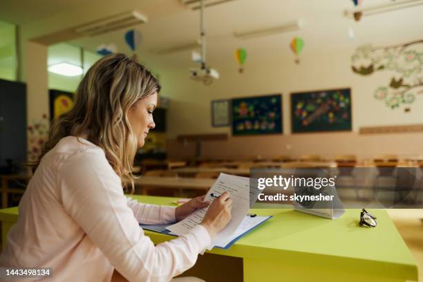 female teacher grading exams in the classroom. - teacher marking exams stock pictures, royalty-free photos & images