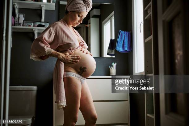 pregnant woman pouring cream on her tummy seen from below - woman in shower tattoo stock pictures, royalty-free photos & images