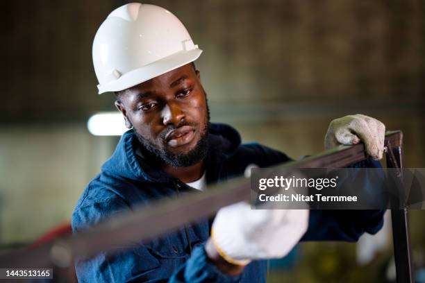 welded seam inspection in metal structure fabrication. front view of a male african american welder checking welded seam accuracy of a metal frame parts surface during welds in metal fabrication. - surfacing stock pictures, royalty-free photos & images