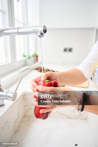 woman cleaning under the tap a red pepper for paella - ingredientes stock-fotos und bilder