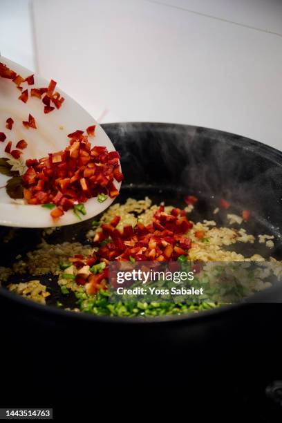 housewife pouring red pepper into a pan to make paella - ingredientes stock-fotos und bilder