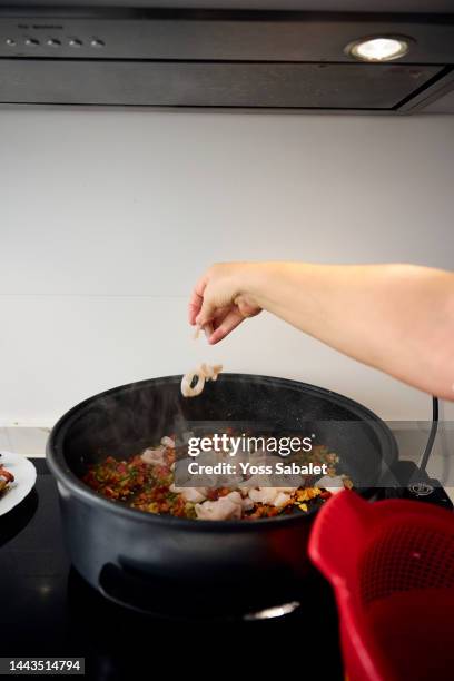 housewife adding pieces of squid to the paella - ingredientes stock-fotos und bilder