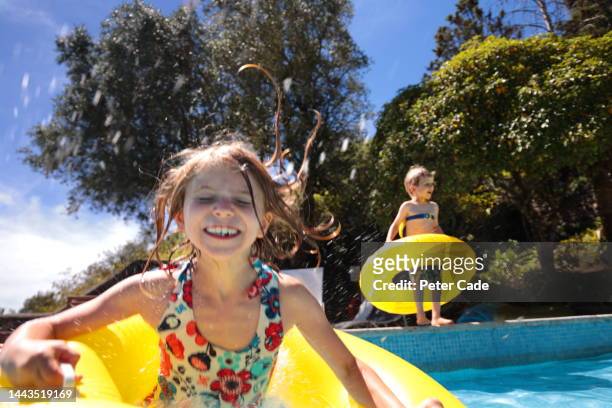girl and boy jumping into swimming pool - tube girl stock-fotos und bilder