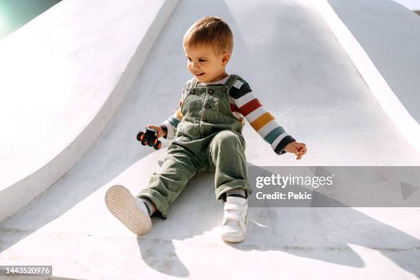 cute little boy sliding on a playground with a car toy in his hands - beautiful blonde babes stock pictures, royalty-free photos & images