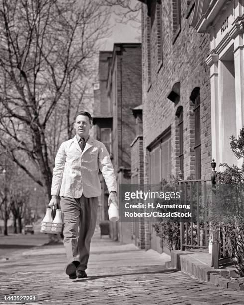 1940s Milkman Walking Up Brick Paved Street Wearing White Jacket Carrying Glass Bottles Of Milk Ready For Door Step Delivery