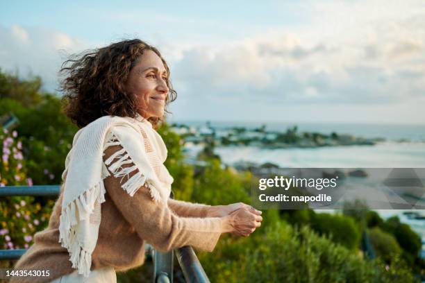 smiling mature woman looking out at the sunset over the ocean - oudere vrouwen stockfoto's en -beelden