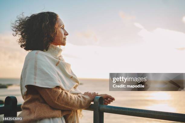 mujer madura viendo la puesta de sol sobre el océano - think fotografías e imágenes de stock