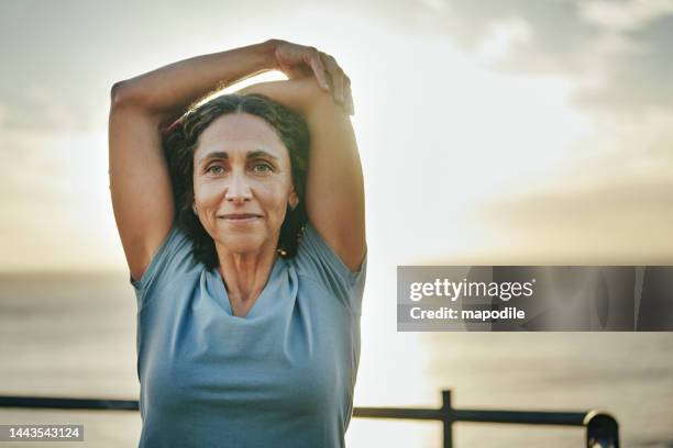 smiling mature woman stretching before a run by the ocean - woman stretching sunset bildbanksfoton och bilder