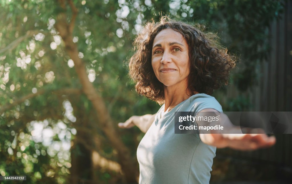 Mulher madura sorridente que faz yoga fora em um parque no verão