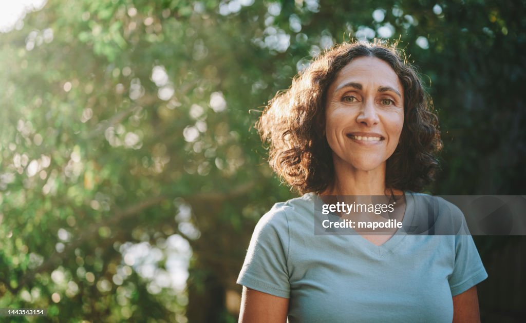 Lächelnde reife Frau, die im Sommer in einem Park im Freien steht