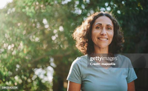 mujer madura sonriente parada en un parque al aire libre en el verano - mujer feliz fotografías e imágenes de stock