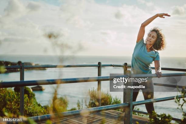 fit mature woman stretching by the ocean before a run - strekken stockfoto's en -beelden