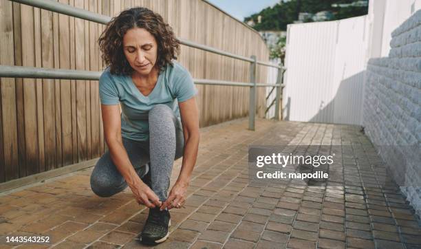 une femme mûre en forme attachant ses chaussures pour courir dehors en été - 50 feet photos et images de collection