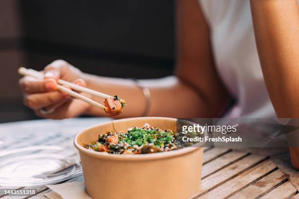 a close up view of an anonymous woman having lunch from a cardboard food container using chopsticks - eetstokje stockfoto's en -beelden
