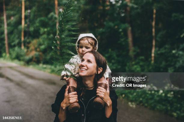 girl holding twig sitting on shoulders of smiling mother in rainy forest - women taking showers stock pictures, royalty-free photos & images