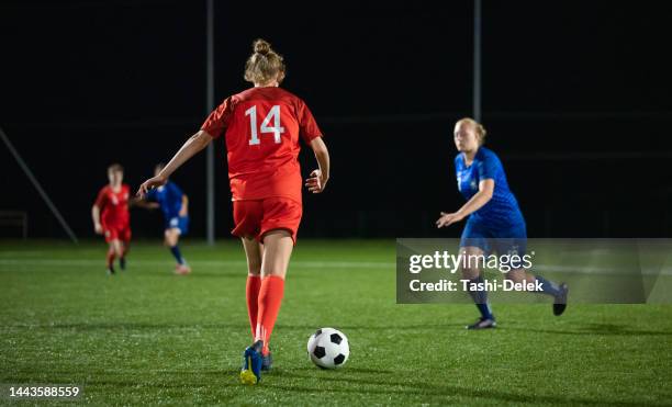 plan d’une joueuse de football déterminée tapant dans le ballon lors d’un match la nuit - essayer de marquer photos et images de collection