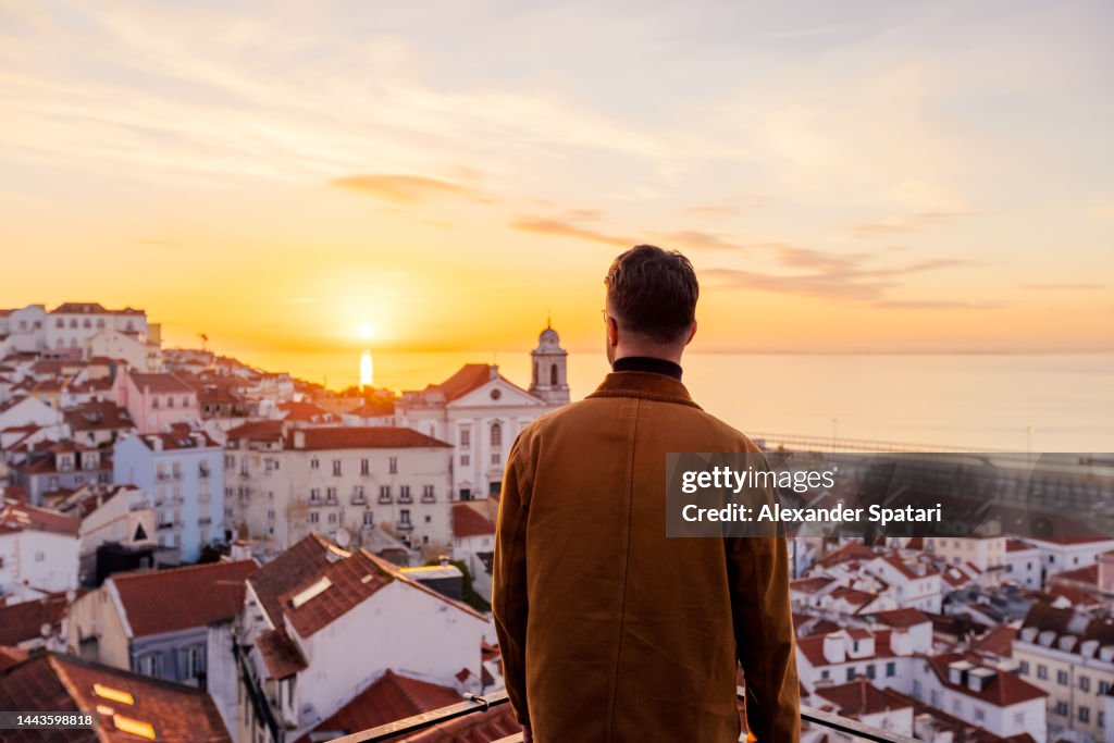Rear view of a man looking at Lisbon skyline at sunrise, Portugal