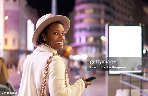 cheerful latin american woman at the city at night using mobile phone. - street light banner stock pictures, royalty-free photos & images