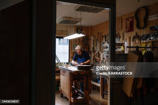 man working at a workshop with musical instruments - plucking an instrument - fotografias e filmes do acervo