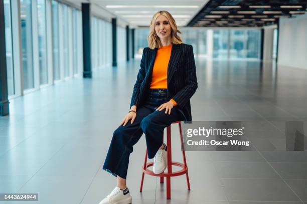portrait of young businesswoman in blazer sitting in a modern office space - ad sales event ストックフォトと画像